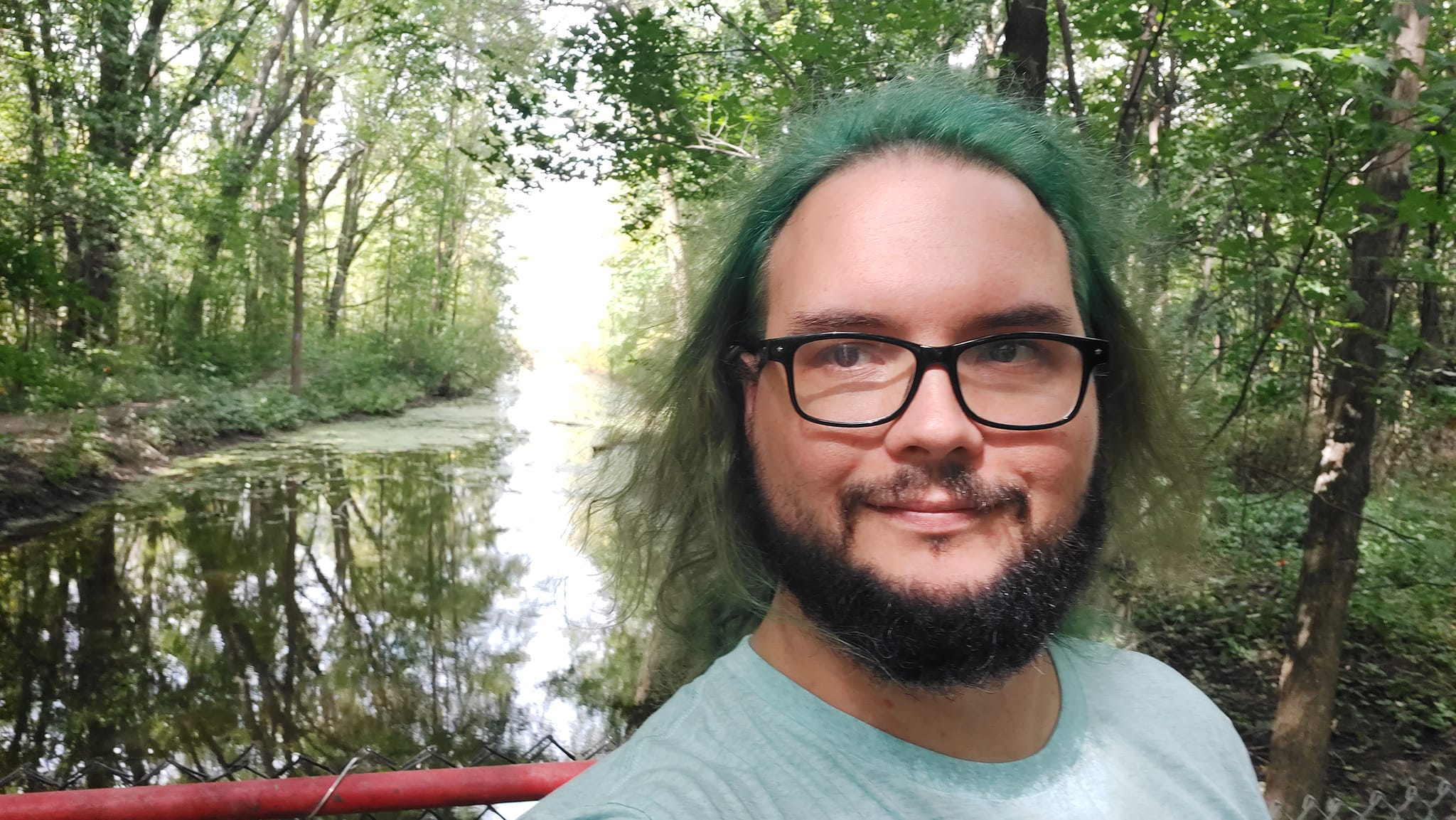 A man with green hair stands on a dam with a channel extending behind him, Photo 3